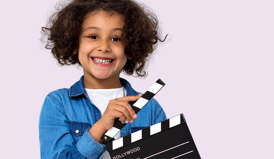 A smiling child smiles holds a clapper.